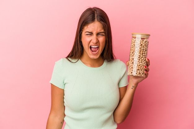 Young caucasian woman holding a chickpeas jar isolated on pink background screaming very angry and aggressive.