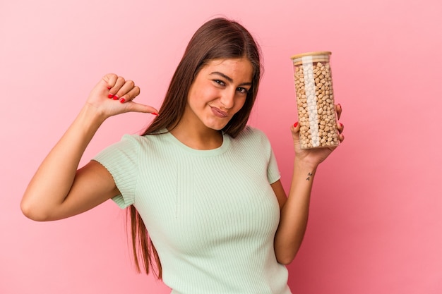 Foto la giovane donna caucasica che tiene un barattolo di ceci isolato sul muro rosa si sente orgogliosa e sicura di sé, esempio da seguire.