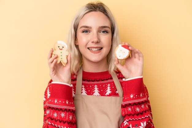 黄色の背景で隔離のクリスマスのクッキーを保持している若い白人女性