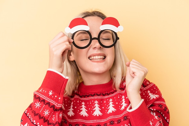 Young caucasian woman holding a christmas props isolated on yellow background