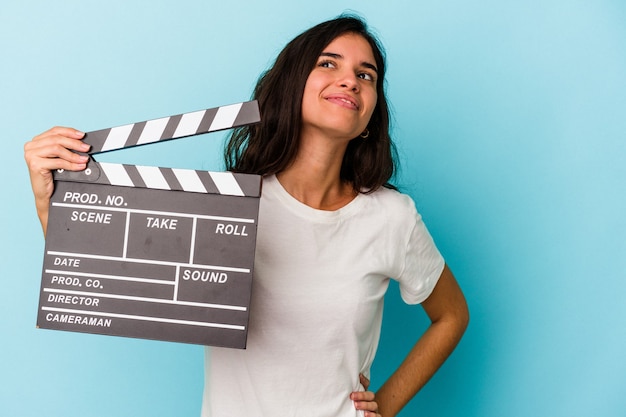 Young caucasian woman holding a clapperboard isolated on blue background dreaming of achieving goals and purposes