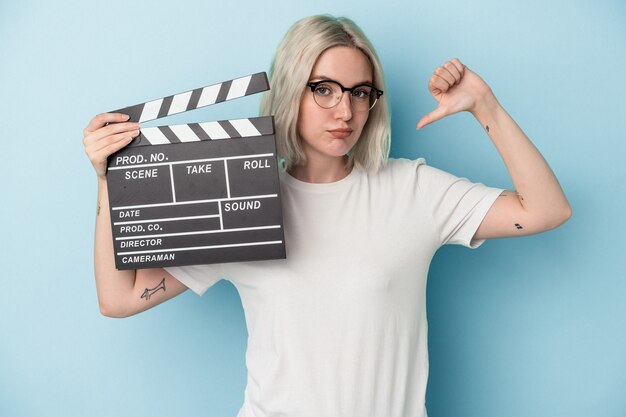 Young caucasian woman holding a clapperboard isolated on blue background feels proud and self confident, example to follow.