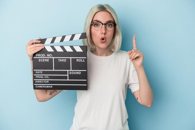 Young caucasian woman holding a clapperboard isolated on blue background having some great idea, concept of creativity.