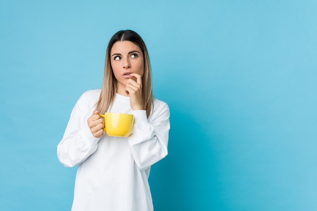 Young caucasian woman holding a coffee cup relaxed thinking about something looking at a copy space.