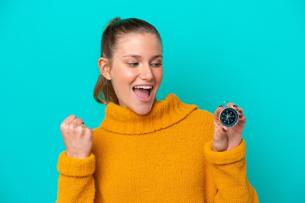 Young caucasian woman holding compass isolated on blue background celebrating a victory