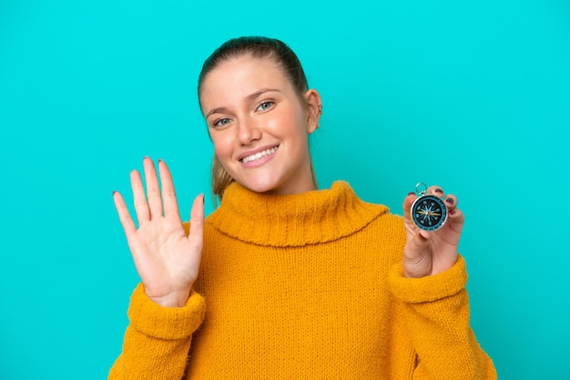 Young caucasian woman holding compass isolated on blue background saluting with hand with happy expression