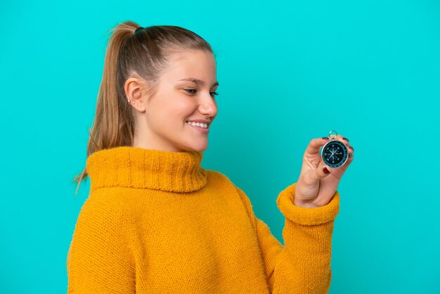 Young caucasian woman holding compass isolated on blue background with happy expression