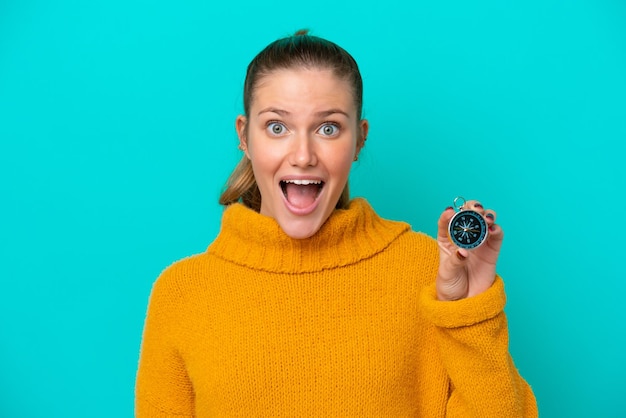 Young caucasian woman holding compass isolated on blue background with surprise and shocked facial expression