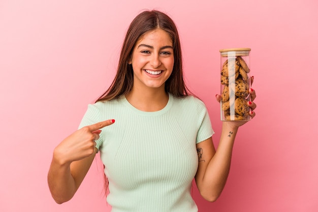 Young caucasian woman holding a cookies jar isolated on pink background person pointing by hand to a shirt copy space, proud and confident
