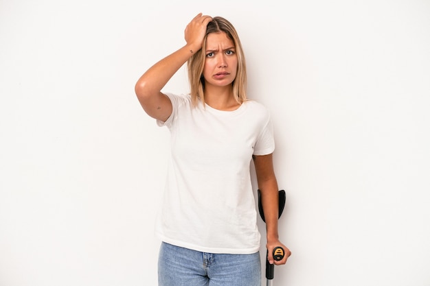 Young caucasian woman holding crutch isolated on white background being shocked, she has remembered important meeting.