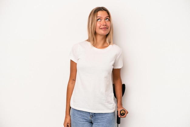 Young caucasian woman holding crutch isolated on white background dreaming of achieving goals and purposes