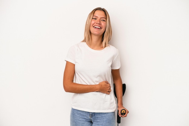 Young caucasian woman holding crutch isolated on white background laughing and having fun.