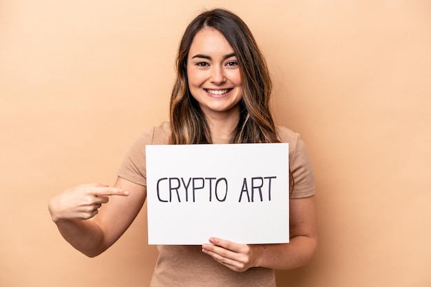 Young caucasian woman holding a crypto art placard isolated on beige background smiling and pointing aside showing something at blank space