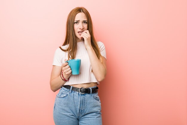 爪をかむ、神経質で非常に不安なカップを保持している若い白人女性。