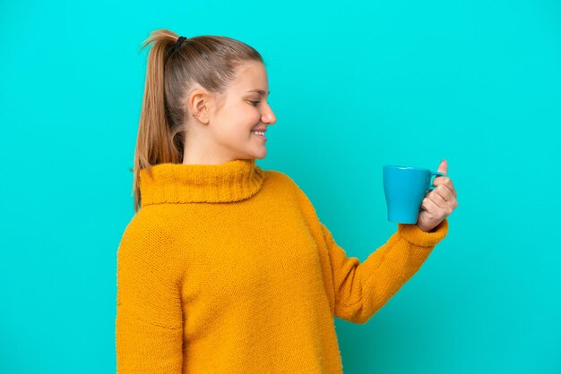 Young caucasian woman holding cup isolated on blue background with happy expression