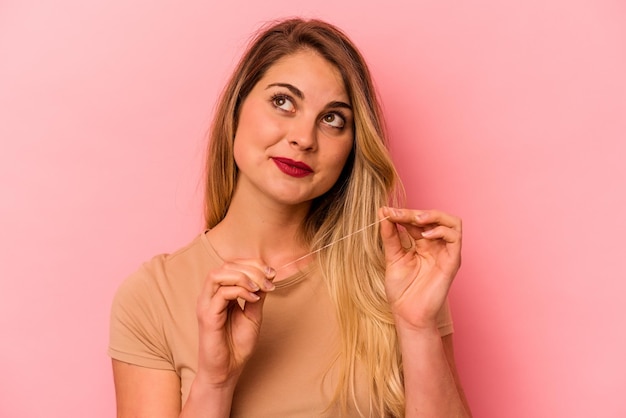 Young caucasian woman holding dental floss isolated on pink background