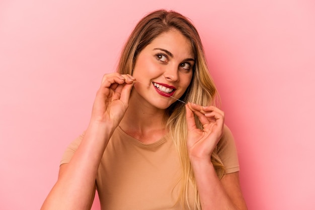 Young caucasian woman holding dental floss isolated on pink background