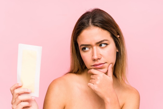 Young caucasian woman holding a depilatory band isolated looking sideways with doubtful and skeptical expression.