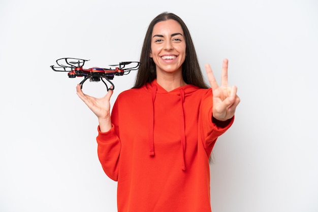 Young caucasian woman holding a drone isolated on white background smiling and showing victory sign