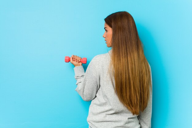 Giovane donna caucasica che tiene un manubrio isolato sull'azzurro