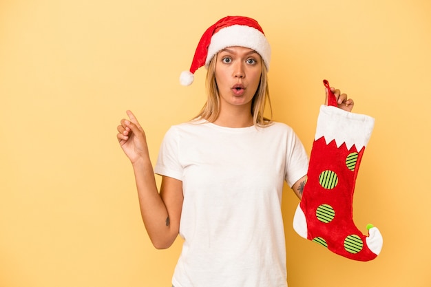 Young caucasian woman holding a elf sock isolated on yellow background pointing to the side