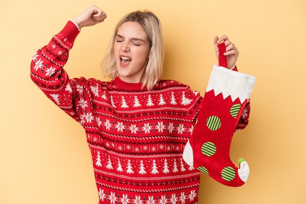 Photo young caucasian woman holding a elf sock isolated on yellow background raising fist after a victory, winner concept.