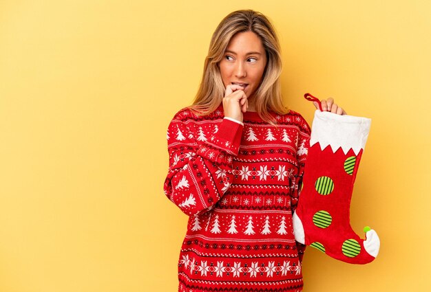 Young caucasian woman holding a elf sock isolated on yellow background relaxed thinking about something looking at a copy space.