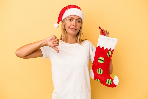 Young caucasian woman holding a elf sock isolated on yellow background showing a dislike gesture, thumbs down. Disagreement concept.