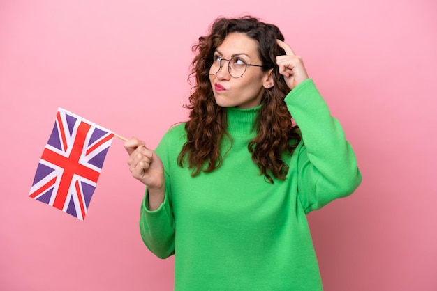 Young caucasian woman holding english flag isolated on pink background having doubts and with confuse face expression