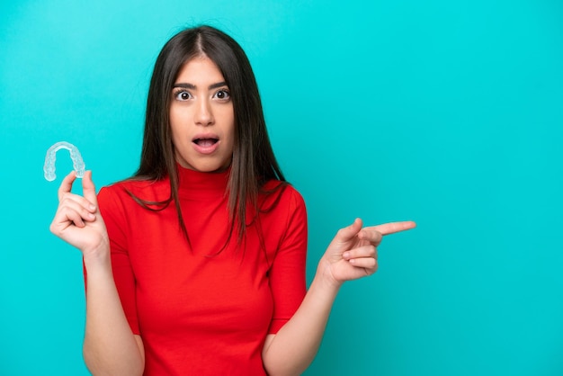 Young caucasian woman holding a envisaging isolated on blue background surprised and pointing side