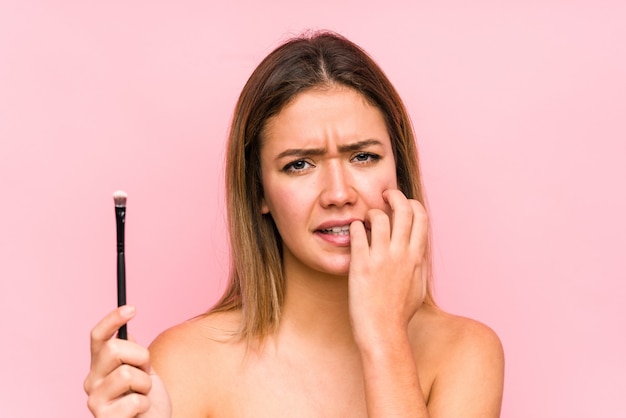 Young caucasian woman holding a eyebrush isolated biting fingernails, nervous and very anxious.