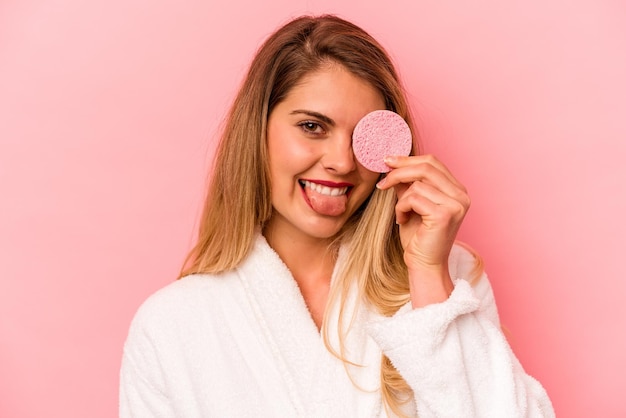 Young caucasian woman holding facial sponge isolated on pink background