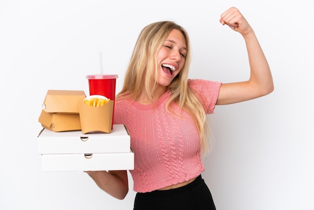 Young caucasian woman holding fat food isolated on blue background celebrating a victory