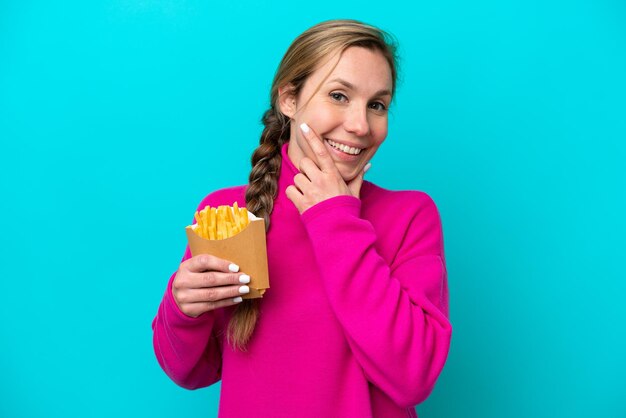 Giovane donna caucasica azienda patatine fritte isolate su sfondo blu felice e sorridente