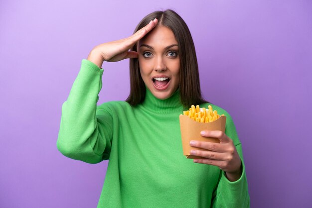 Young caucasian woman holding fried chips on purple background with surprise expression