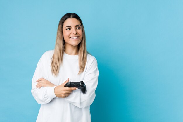組んだ腕に自信を持って笑顔のゲームコントローラーを保持している若い白人女性。