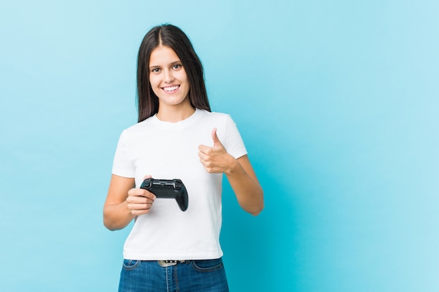 Young caucasian woman holding a game controller smiling and raising thumb up