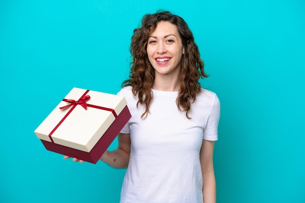 Young caucasian woman holding a gift isolated on blue background smiling a lot