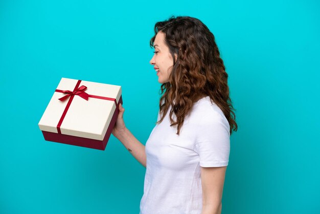 Young caucasian woman holding a gift isolated on blue background with happy expression