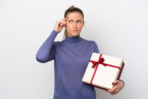 Foto giovane donna caucasica in possesso di un regalo isolato su sfondo bianco con dubbi e con un'espressione facciale confusa