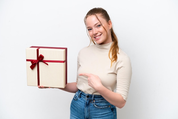 Young caucasian woman holding a gift isolated on white background and pointing it