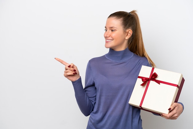 Giovane donna caucasica in possesso di un regalo isolato su sfondo bianco che indica il lato per presentare un prodotto