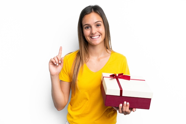 Young caucasian woman holding a gift isolated on white background pointing up a great idea