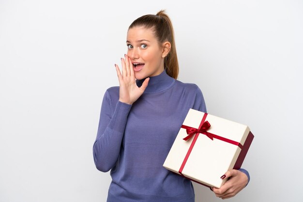 Young caucasian woman holding a gift isolated on white background whispering something