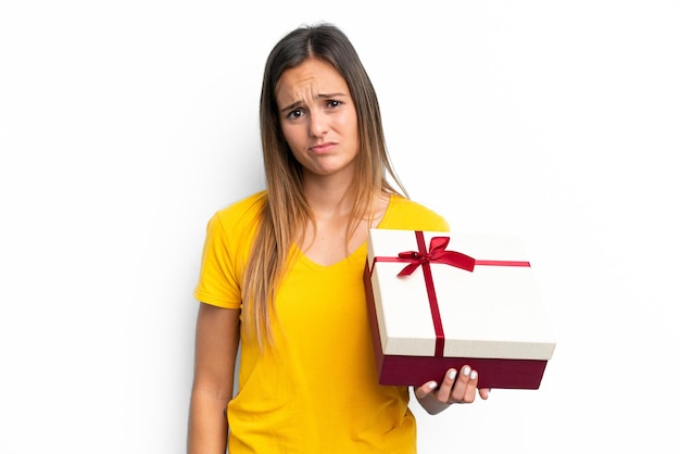 Young caucasian woman holding a gift isolated on white background with sad expression