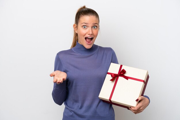 Young caucasian woman holding a gift isolated on white background with shocked facial expression