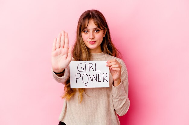 Photo young caucasian woman holding a girl power placard isolated on pink background standing with outstretched hand showing stop sign, preventing you.