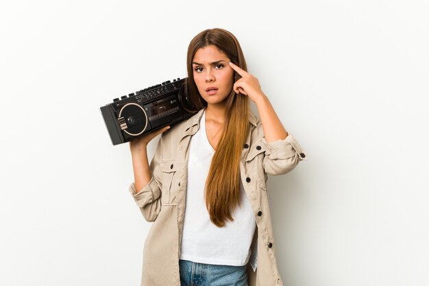 Young caucasian woman holding a guetto blaster showing a disappointment gesture with forefinger.