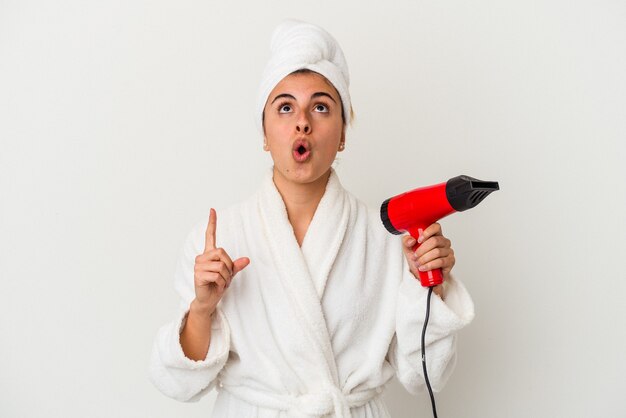 Young caucasian woman holding an hair dryer isolated on white pointing upside with opened mouth.