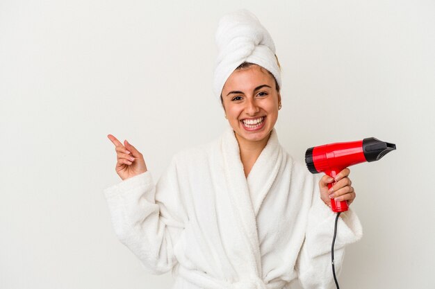 Young caucasian woman holding an hair dryer isolated on white smiling and pointing aside, showing something at blank space.